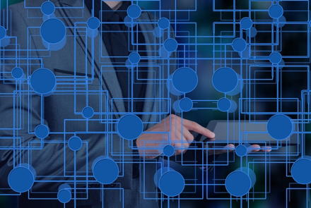 Persona uzvalkā izmanto planšetdatoru, uz kura ir zilas, savstarpēji savienotas ķēdes veida līnijas un mezgli, kas simbolizē tehnoloģiju un digitālos tīklus.