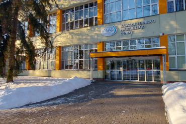 Dzeltena un oranža ēka ar lieliem logiem un sniegotu apkārtni. Ieejai ir stikla durvis, virs kurām ir uzraksts VAVARU TEHNISKO PALĪGLĪDZEKĻU CENTRS.