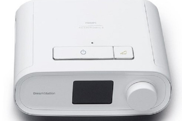 Balts Philips DreamStation CPAP aparāts ar displeja ekrānu, lielu apaļu ciparnīcu un ieslēgšanas pogu uz augšējā paneļa.