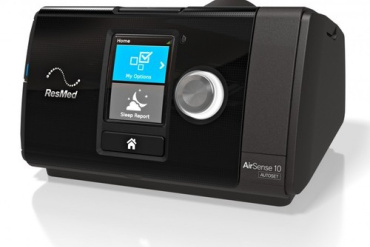 Melns ResMed AirSense 10 CPAP aparāts ar digitālo ekrānu un vadības slēdzi, kas paredzēts miega apnojas terapijai, atrodas uz balta fona.